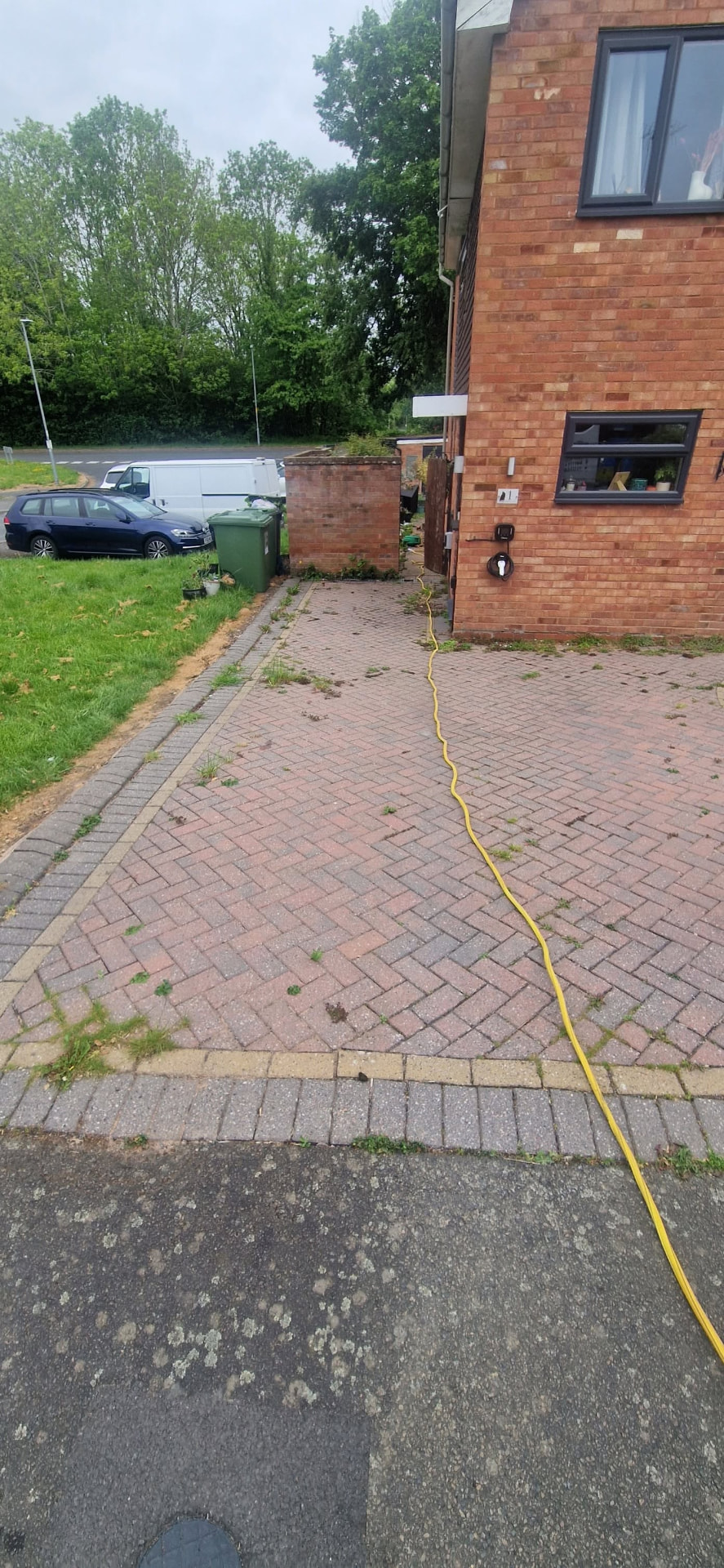 Front block paved driveway with weeds through the joints before cleaning