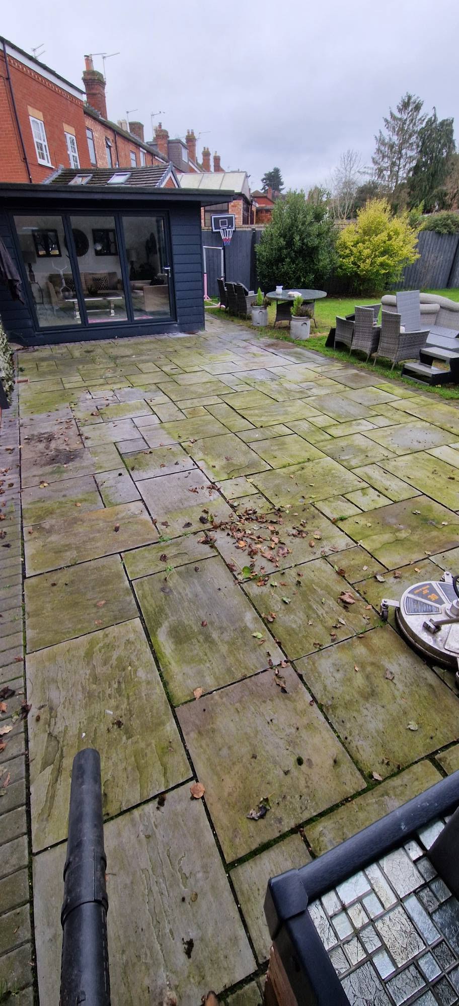 Large rear patio thick with green moss and fallen leaves before pressure washing
